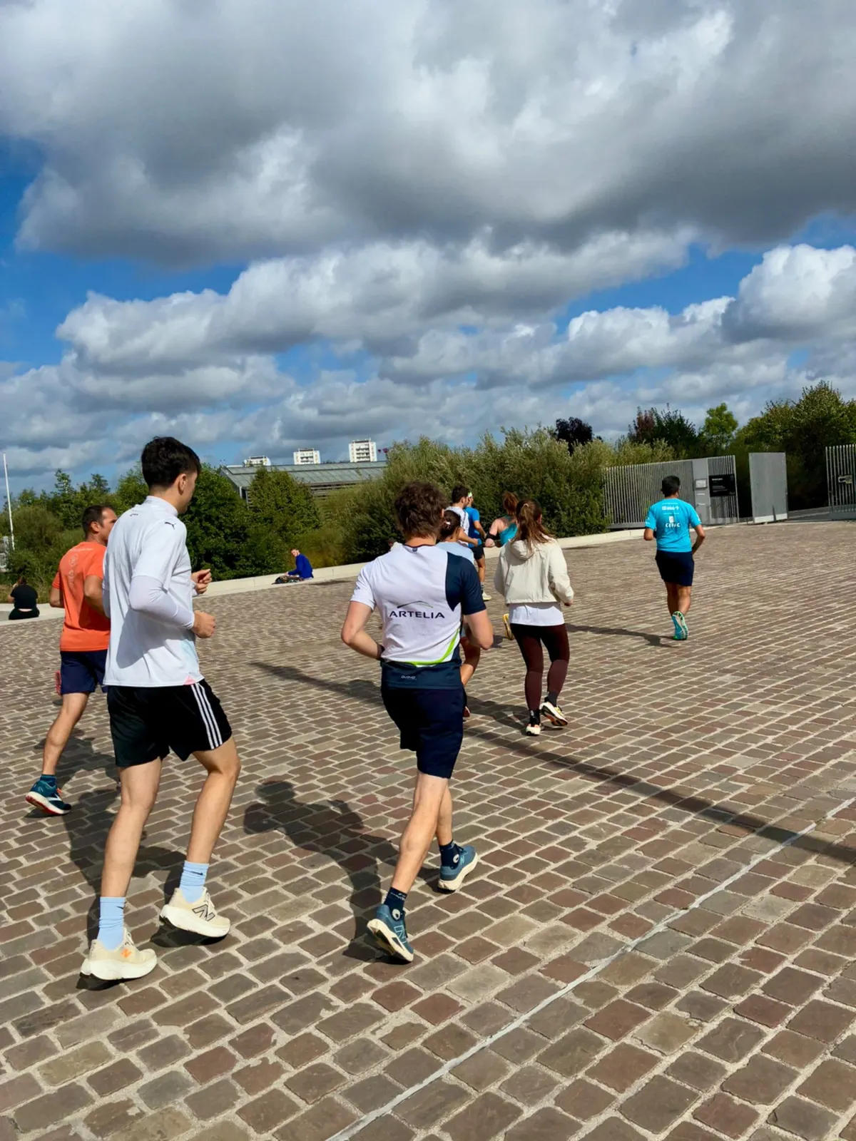 Des collaborateurs d'Artelia courent ensemble sur une esplanade pavée, sous un ciel nuageux