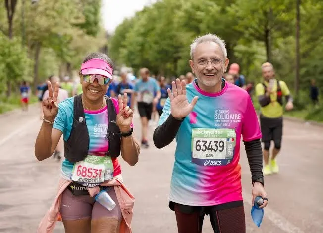 Deux coureurs aux dossards solidaires saluent en souriant pendant le Marathon de Paris