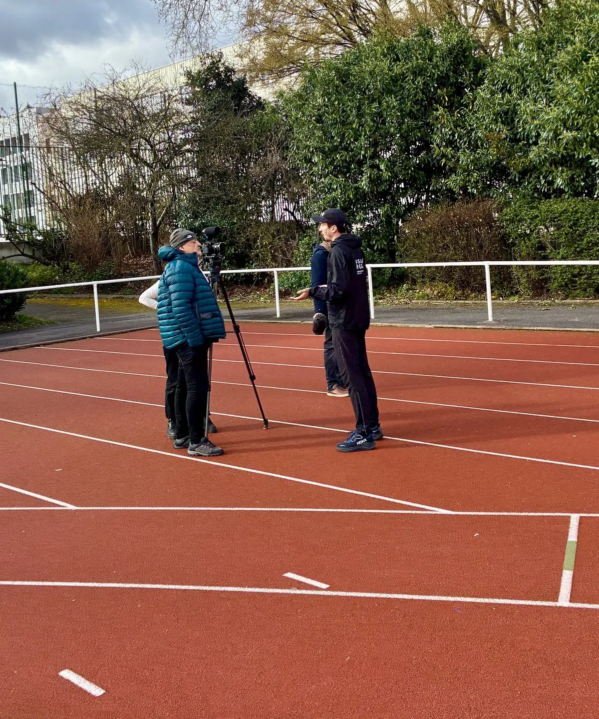Un coach LE FOOTING interviewé face caméra sur une piste d'athlétisme