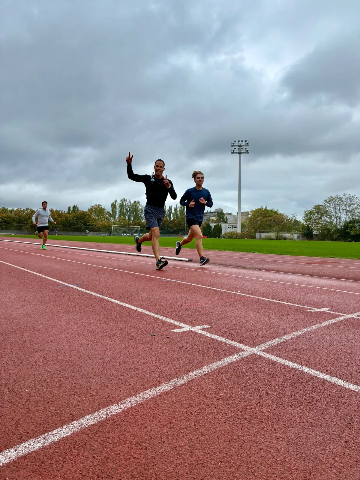 Des coureurs tout sourire sur une piste d'athlétisme, l'un fait le signe de la victoire
